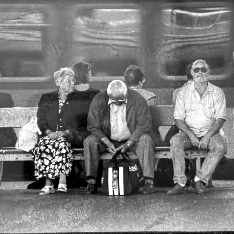Schwarz-weiße Fotografie von 1999: Wartende Menschen auf einer Bahnsteigbank, dahinter ein fahrender Zug